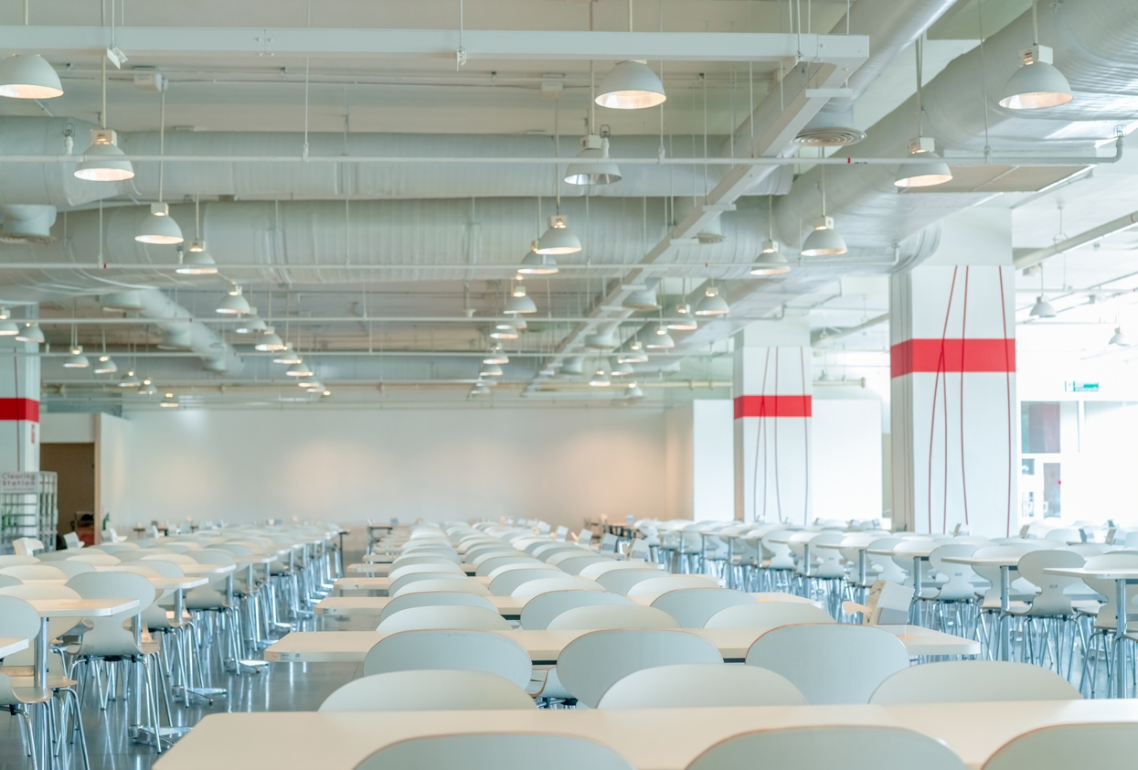 Empty white chair and table in commercial cafeteria breakroom. Air duct, air conditioner pipe and fire sprinkler system. Ventilation system. Building interior. Ceiling lamp light. Interior architecture