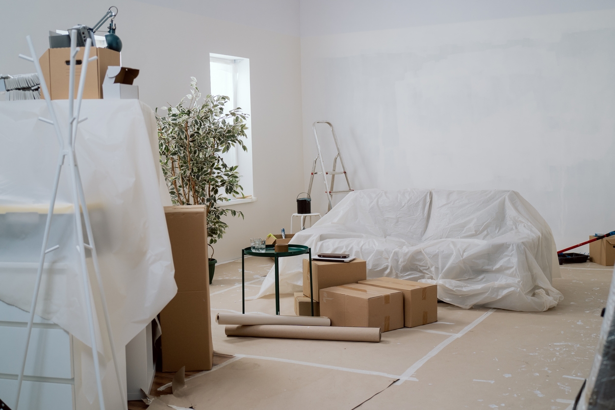 Interior of the room during renovation painting walls with ladder, floor and couch protected with foil cardboard, moving