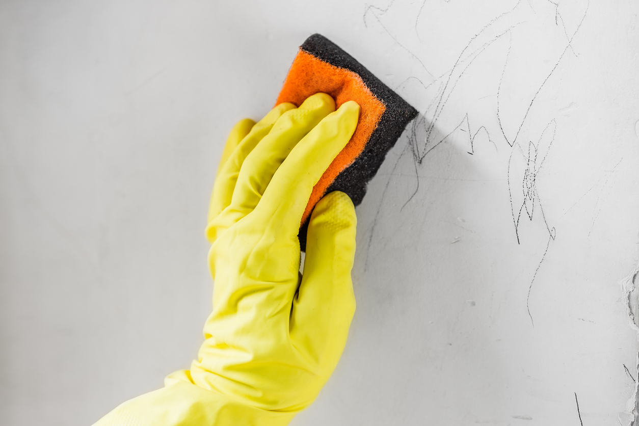 Woman cleaning child drawings from the white wall